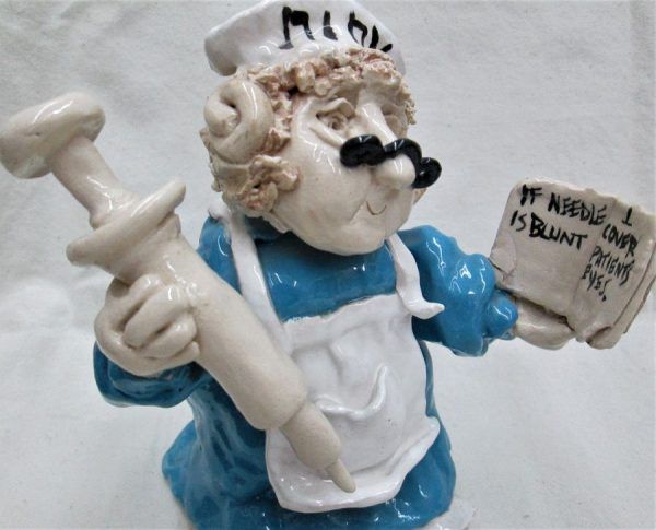Handmade glazed ceramic a shabby Jewish nurse sculpture learning how to treat patient with needle made by Jacqui Lavon.
