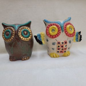 Handmade glazed ceramic brown and white owls sculpture made by T. Labot. White owl wears 12 tribes great priest breast shield.